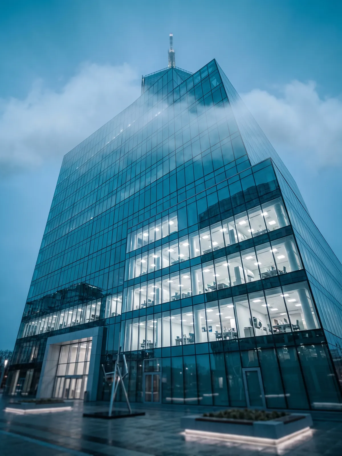 A glass office tower rising into low clouds at blue hour